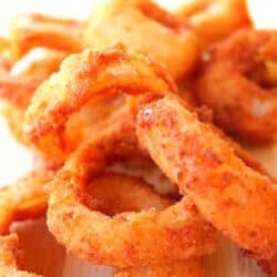 Close-up of a stack of crispy, golden-brown onion rings on a wooden surface.