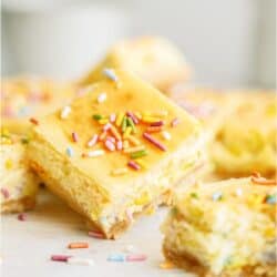 Several cake batter cheesecake bars cut into squares with one slanted on top.