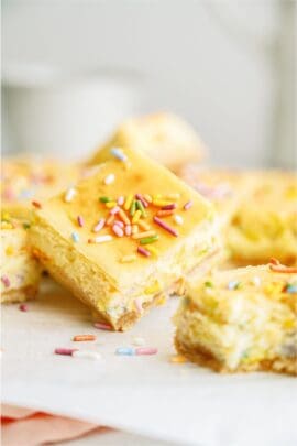 Several cake batter cheesecake bars cut into squares with one slanted on top.