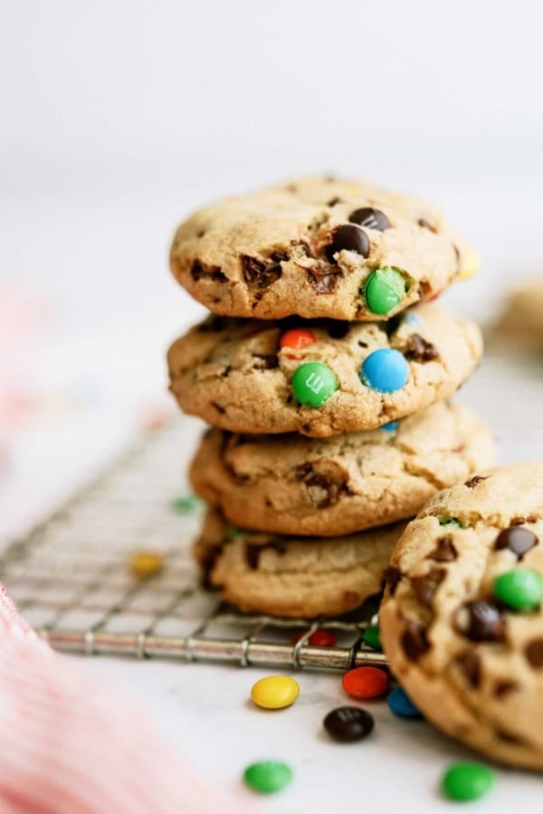 M&M Cookies stacked on a cooling rack with some mini m&m's on the counter.