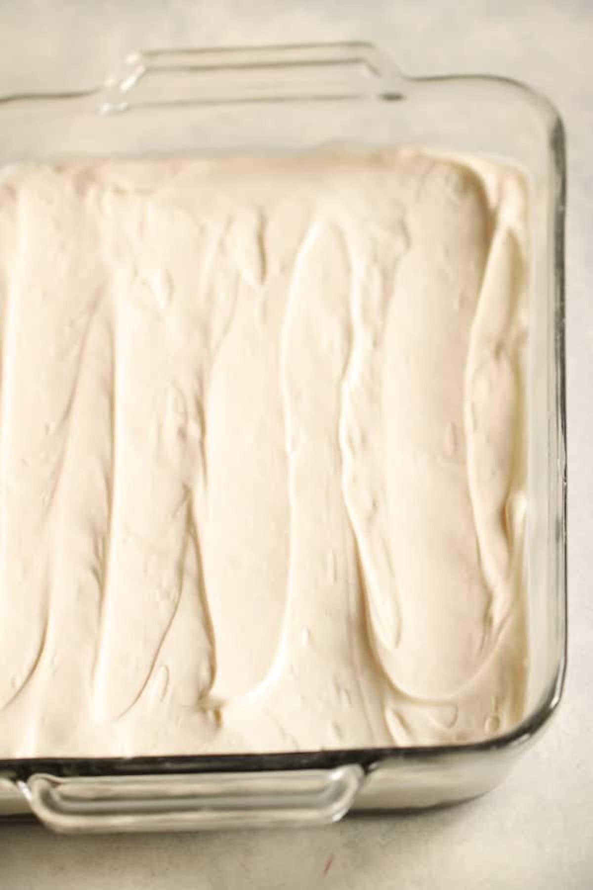 A glass baking dish filled with a smooth, evenly spread layer of white whipped topping or batter.