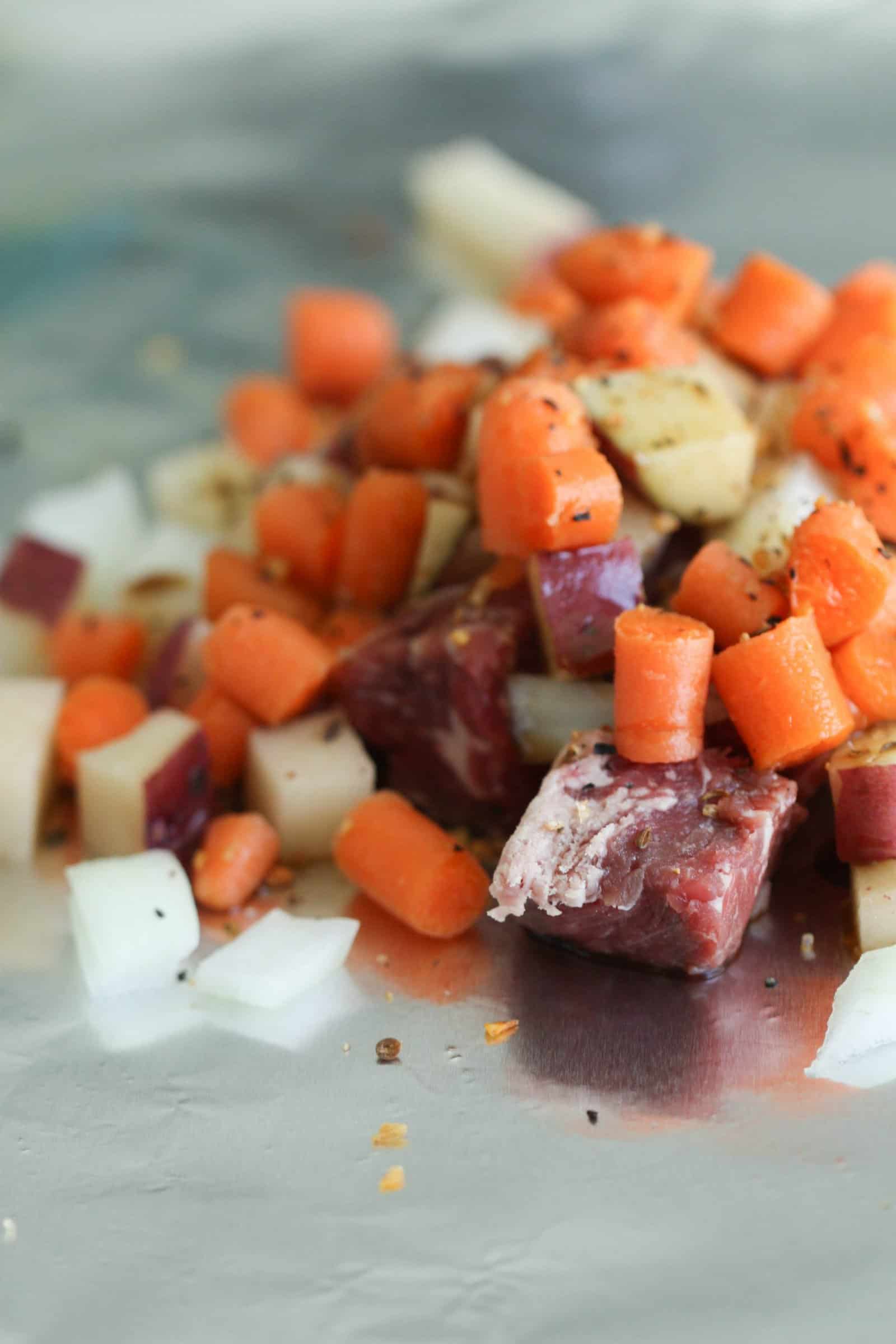 Uncooked beef, carrots, potatoes and onions on a piece of foil
