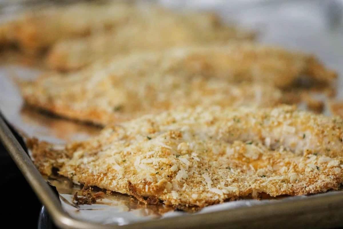 Breaded and baked fish fillets on a foil-lined baking sheet, with a golden-brown, crispy coating.
