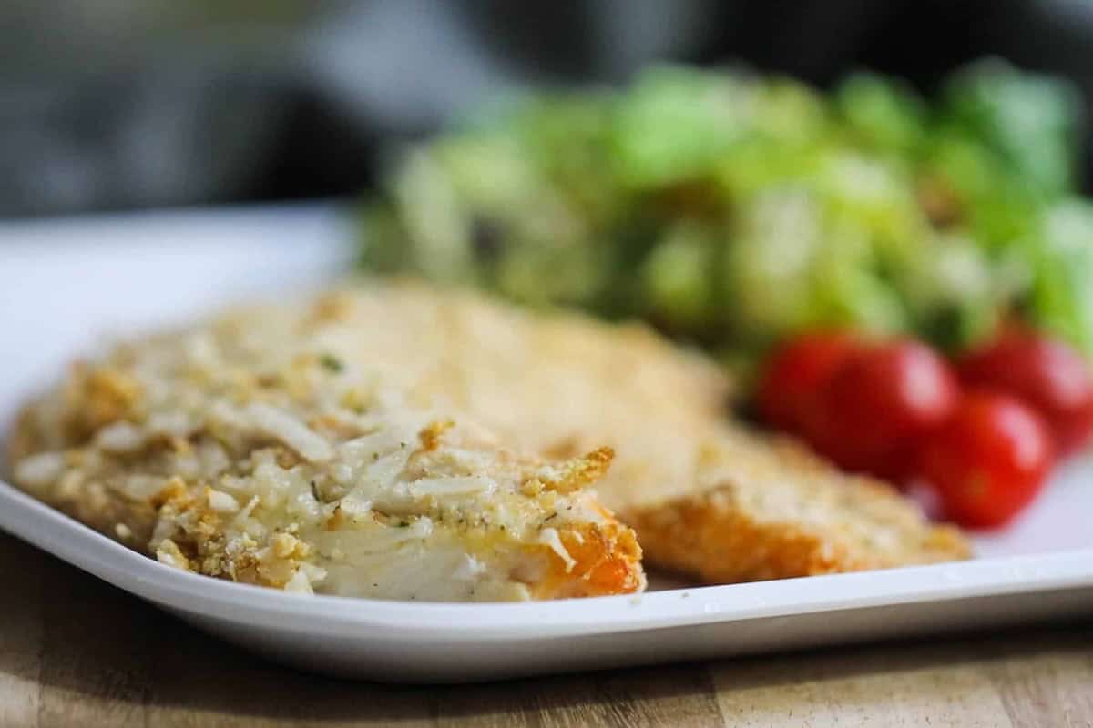 A plate with breaded baked fish fillet, fresh cherry tomatoes, and a green leafy salad.