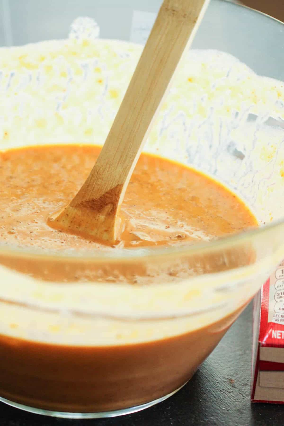 A wooden spoon in a clear bowl of mixed batter next to a box in the background.
