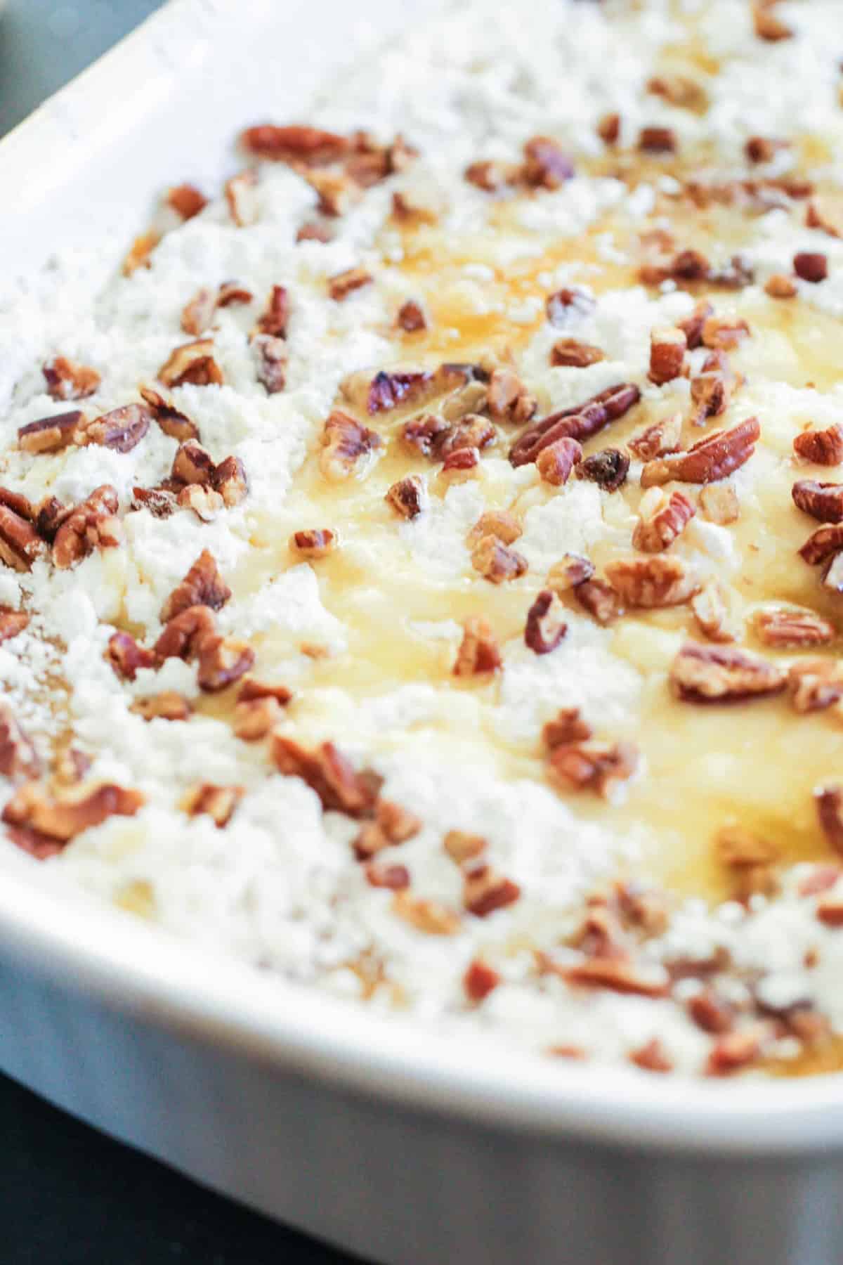 A close-up of a baked dish with a crumbly topping and pecans in a white baking dish.