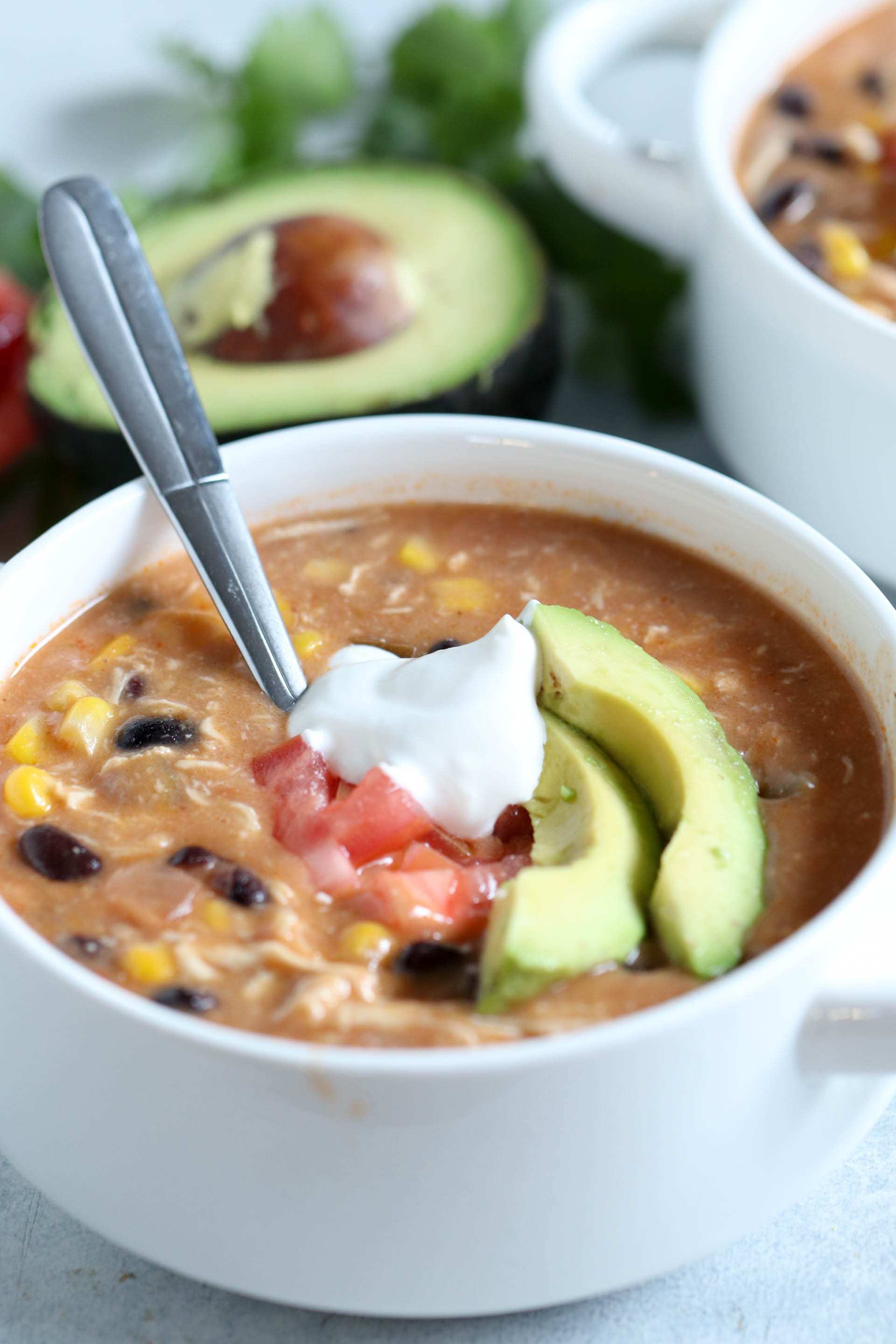 A bowl of Slow Cooker Creamy Chicken Fajita Soup with toppings and a spoon