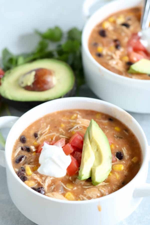 slow cooker creamy chicken fajita soup with tomato, sour cream, and avocado toppings