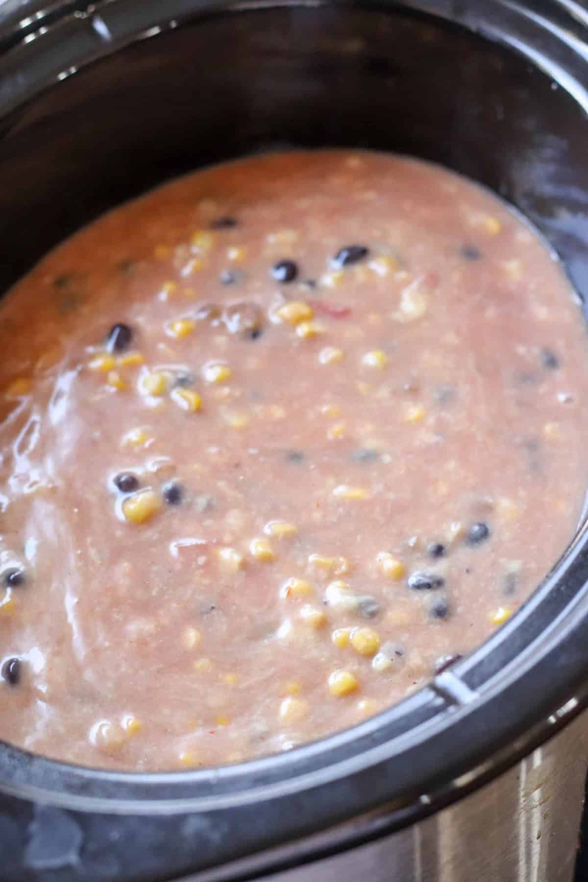 Close-up of a slow cooker filled with a thick soup containing corn, black beans, and a creamy broth.