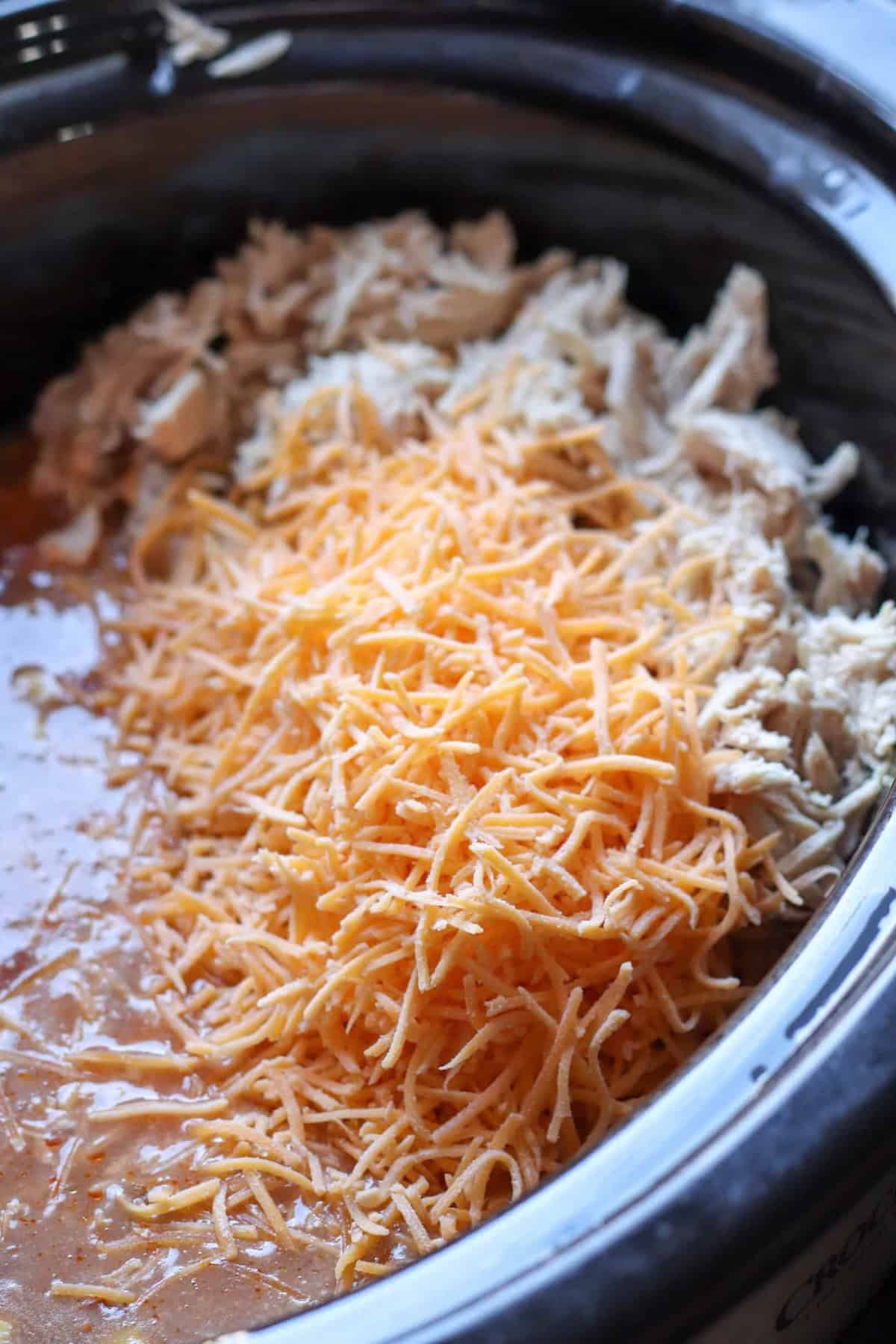 Shredded cheese and shredded chicken in a slow cooker with a creamy sauce.