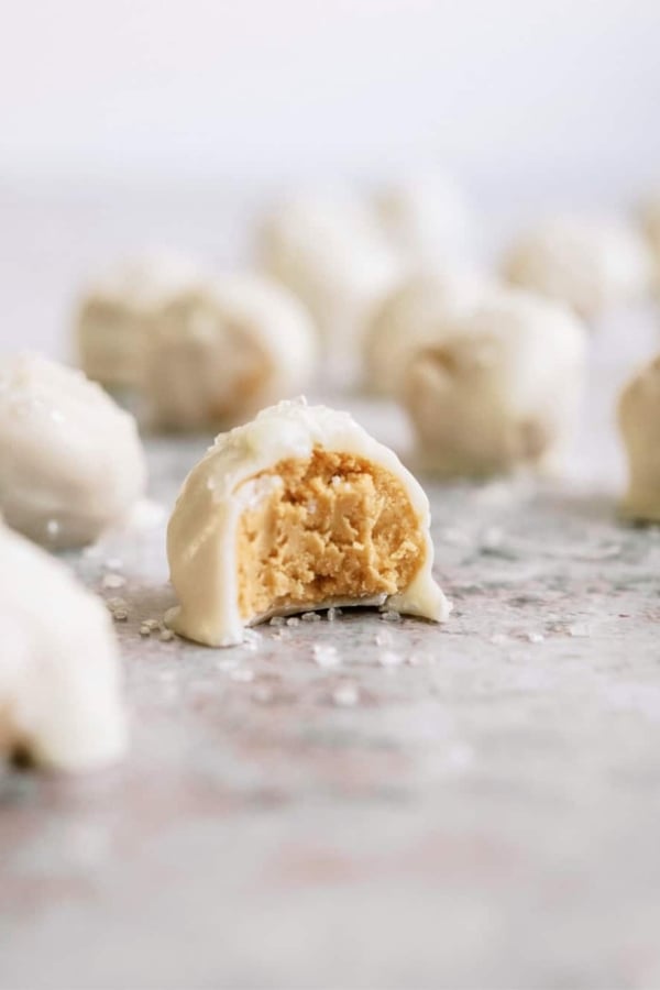 Close-up of white chocolate-covered peanut butter balls, one of which is bitten into, revealing the peanut butter filling.