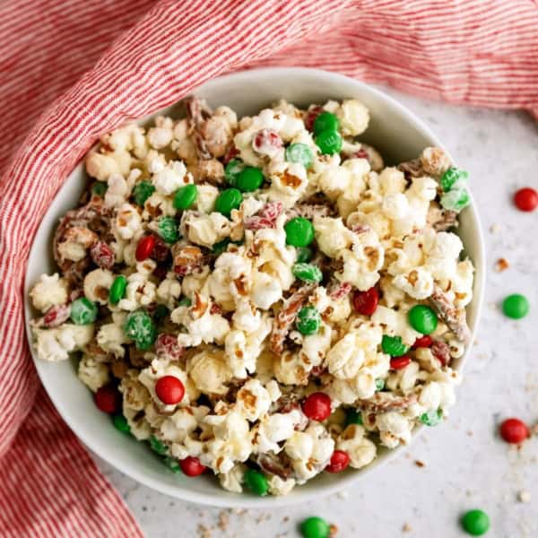 A bowl of popcorn mixed with red and green candy-coated chocolates, placed on a red-striped cloth.