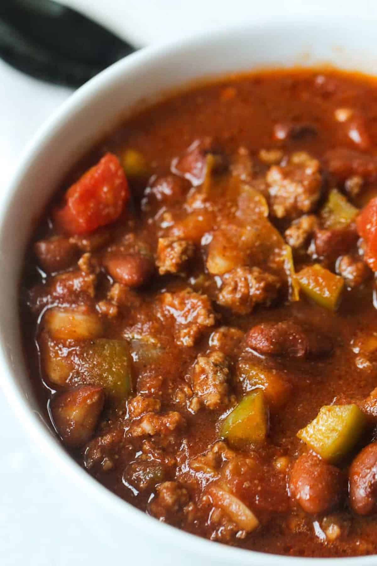 A bowl of chili containing ground beef, beans, diced tomatoes, and chopped green peppers in a thick red sauce.