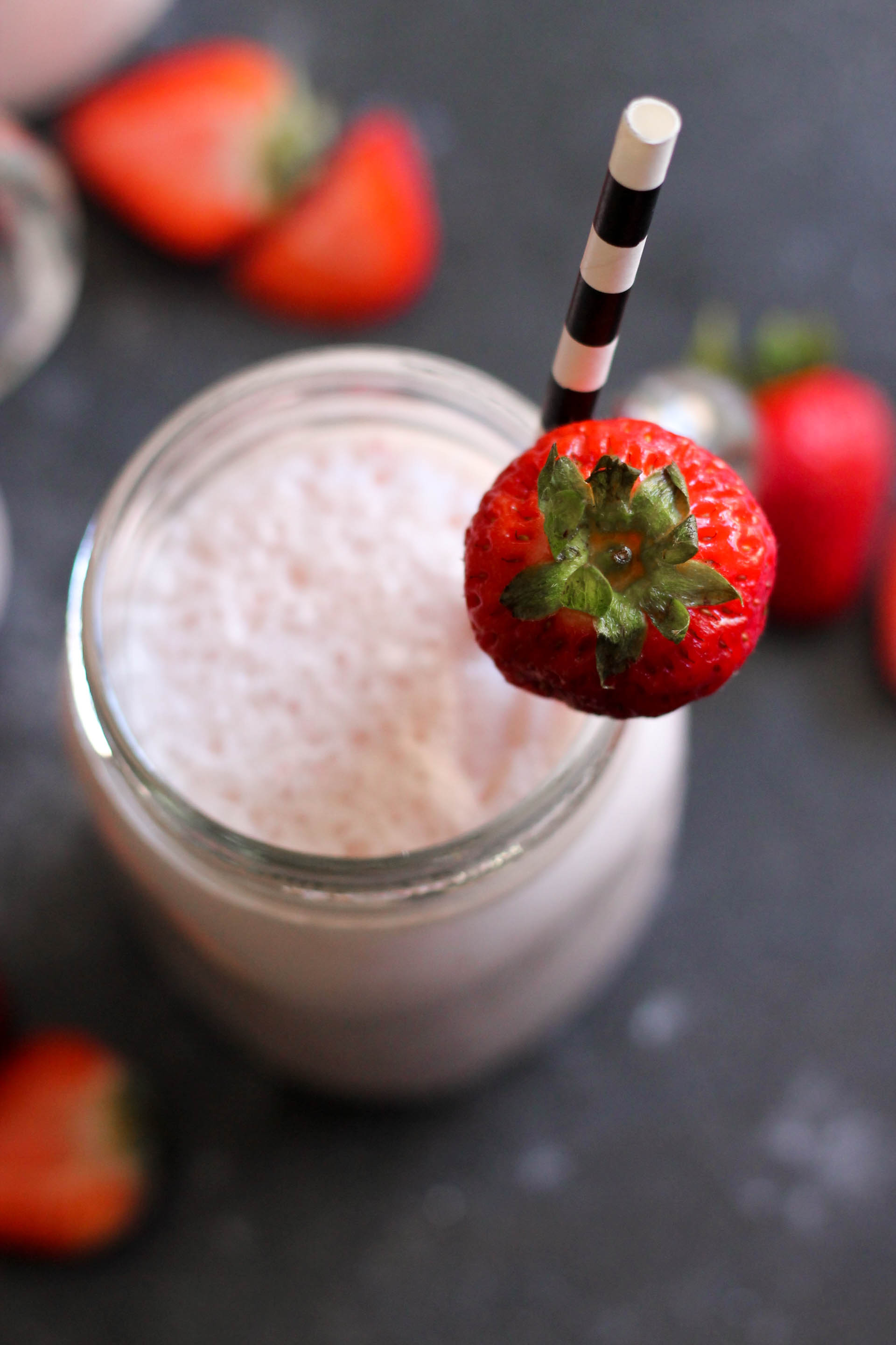 Homemade Strawberry Milkshake in a jar with a straw and fresh strawberry