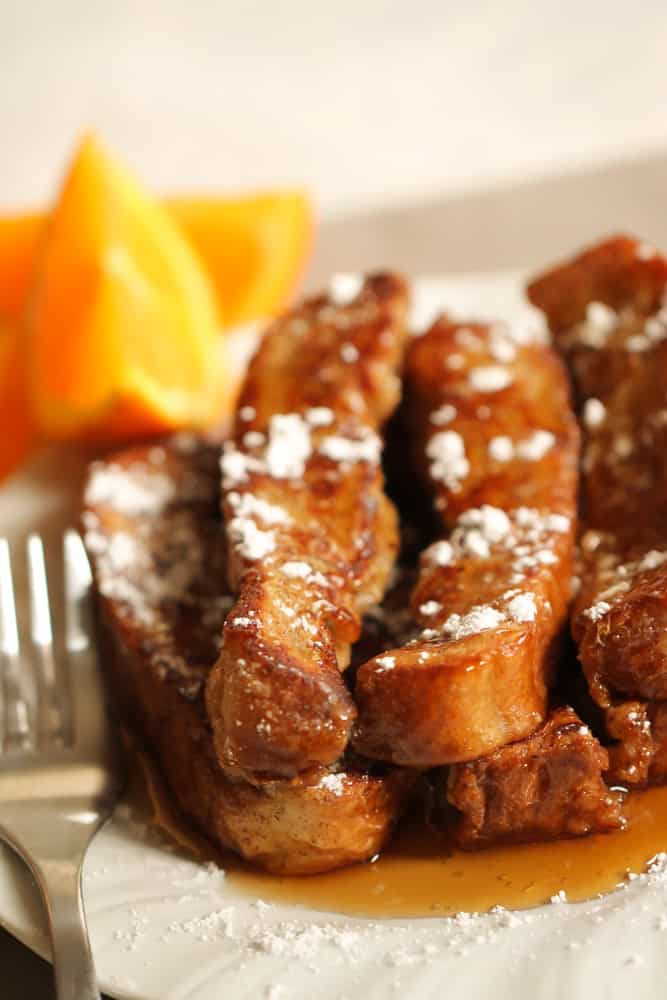 Stack of Homemade French Toast Sticks on a plate with syrup, powdered sugar and a fork