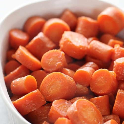 A white dish filled with sliced cooked carrots.