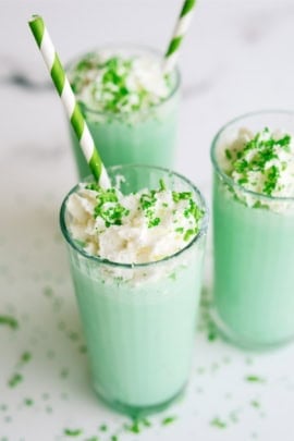 Copycat McDonald's Shamrock Shake in 3 glasses topped with whip cream and green sprinkles. Green and white striped straws in each glass.
