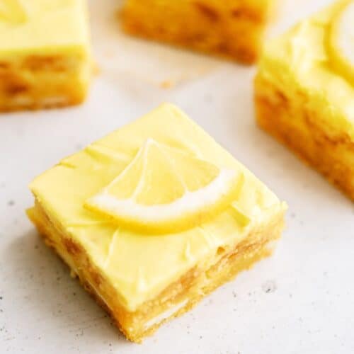 Lemon cookie cheesecake bars cut into squares topped with slices of lemon.