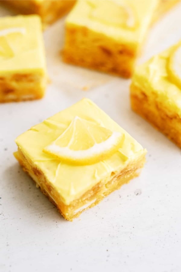 Lemon cookie cheesecake bars cut into squares topped with slices of lemon.
