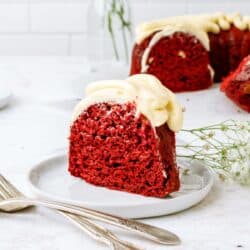 A slice of red velvet bundt cake recipe on a plate with the remaining cake in the background.