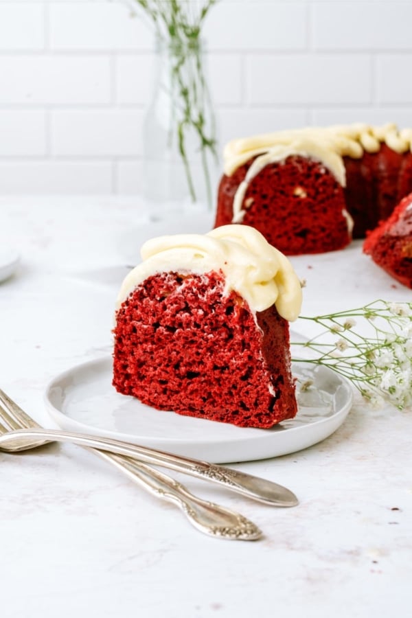 A slice of red velvet bundt cake recipe on a plate with the remaining cake in the background.