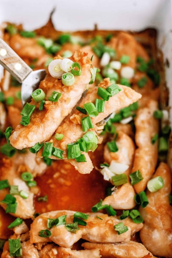 Baked Honey Chicken Tenders in a pan with a spatula lifting 2 tenders out of the baking dish.