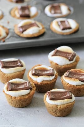 Mini S'mores cups with golden graham cracker crusts, topped with melted marshmallows and chocolate pieces.