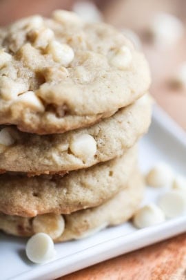4 White Chocolate Macadamia Nut Cookies stacked on a baking sheet with white chocolate chips sprinkled around the bottom.
