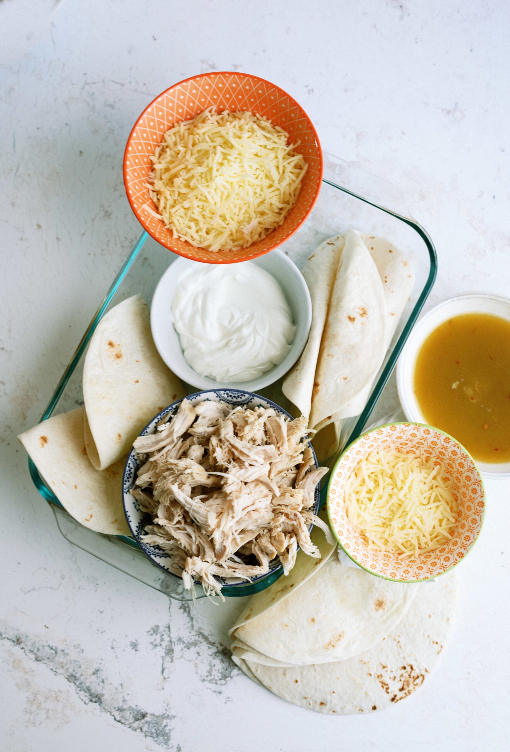 the raw ingredients needed to make this dish: cheese, sour cream, tortillas, green enchilada sauce, cooked chicken
