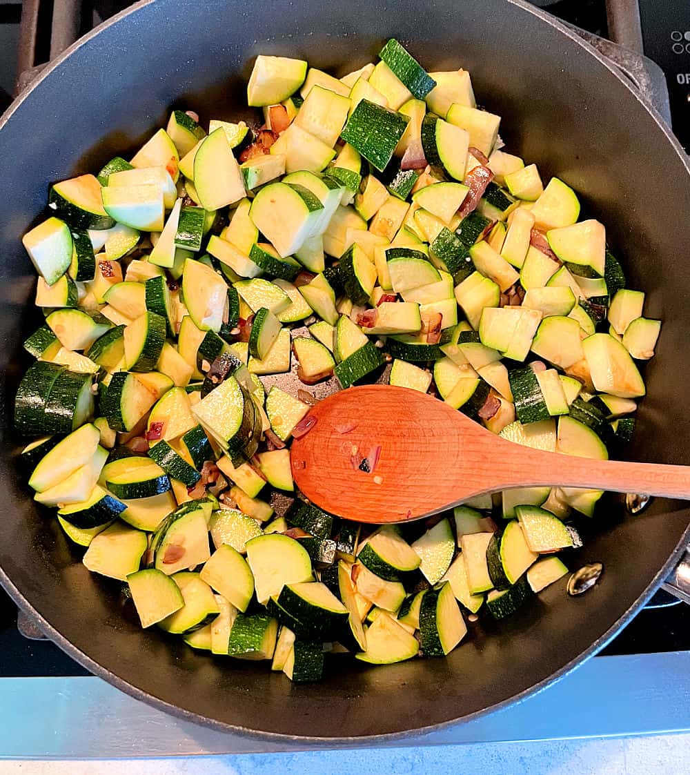 Large skilled with ingredients for Zucchini Corn Parmesan Bake mixed together with wooden spoon