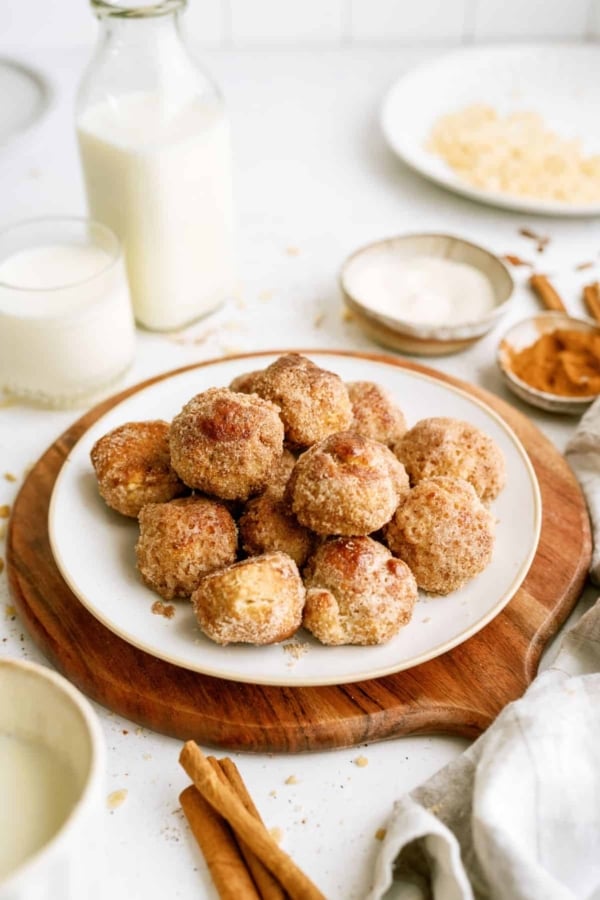 Cinnamon breakfast bites stacked on a plate with a cutting board underneath. A glass of milk and a bottle of milk on the side.