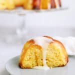 A slice of pineapple poke bundt cake on a plate with the remaining bundt cake in the background.