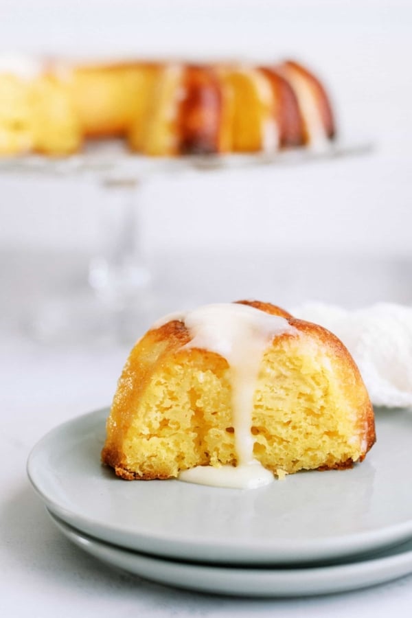 A slice of pineapple poke bundt cake on a plate with the remaining bundt cake in the background.