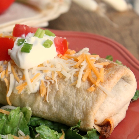 Baked chimichanga topped with sour cream, onion, cheese and tomato