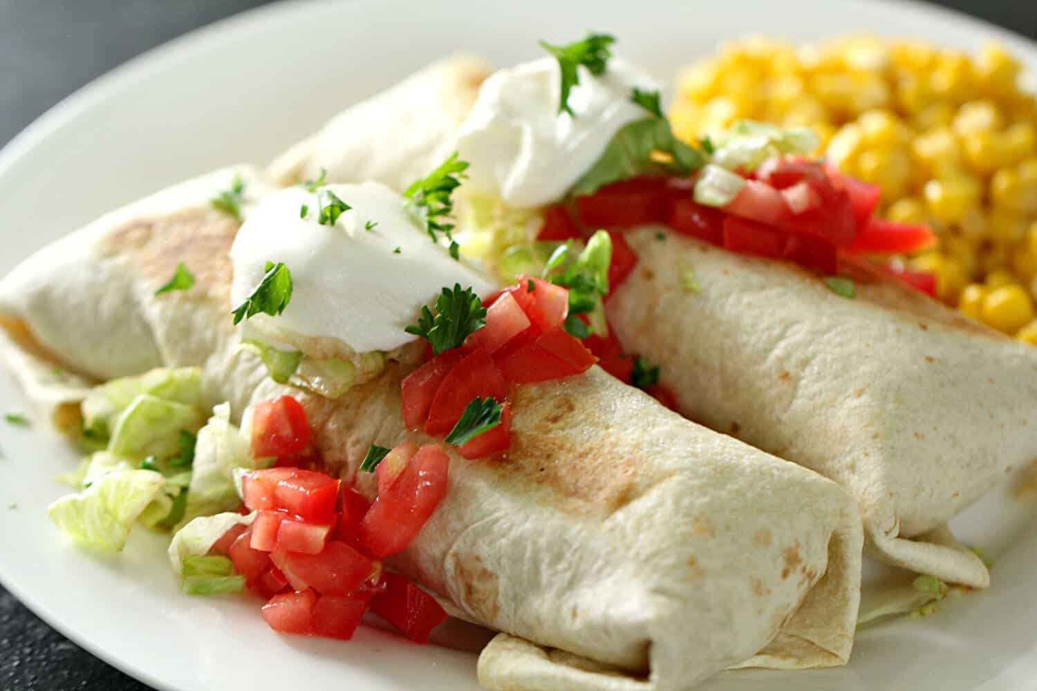 Baked Sweet Pork Chimichangas on a plate served with a side of corn