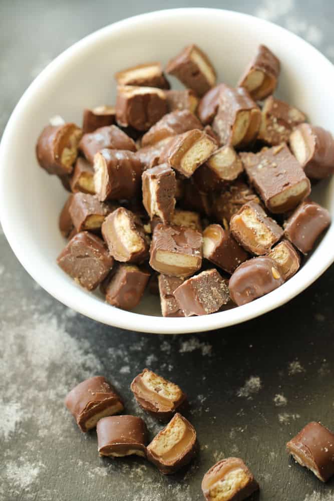 A bowl with chopped up twix miniature candy bard. Some pieces laying on the counter outside of the bowl.