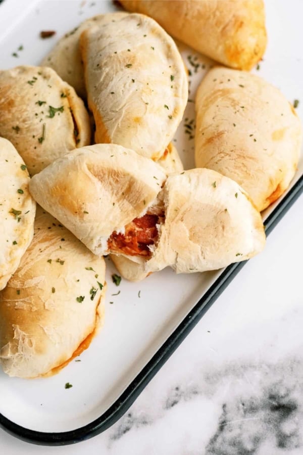 Baked Pizza Pockets on a white serving tray with on split in half to see the inside.