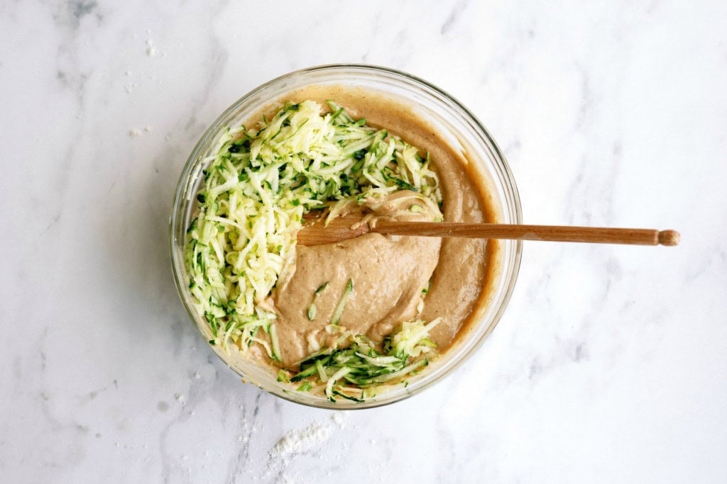 Mixing cake batter with fresh zucchini in a mixing bowl with a wooden spoon.