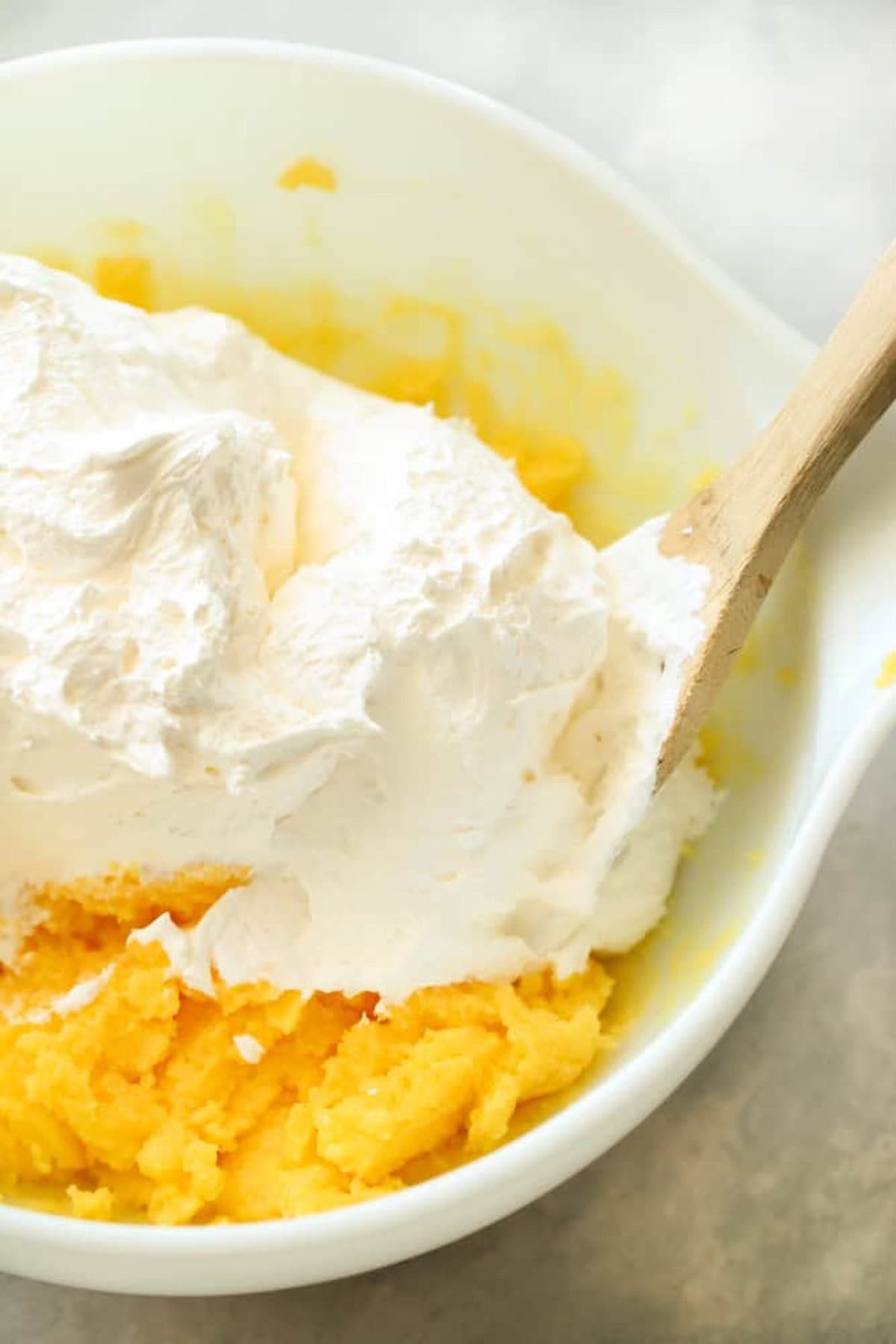 Pudding and Cool Whip being mixed together with a wooden spoon in a large mixing bowl.
