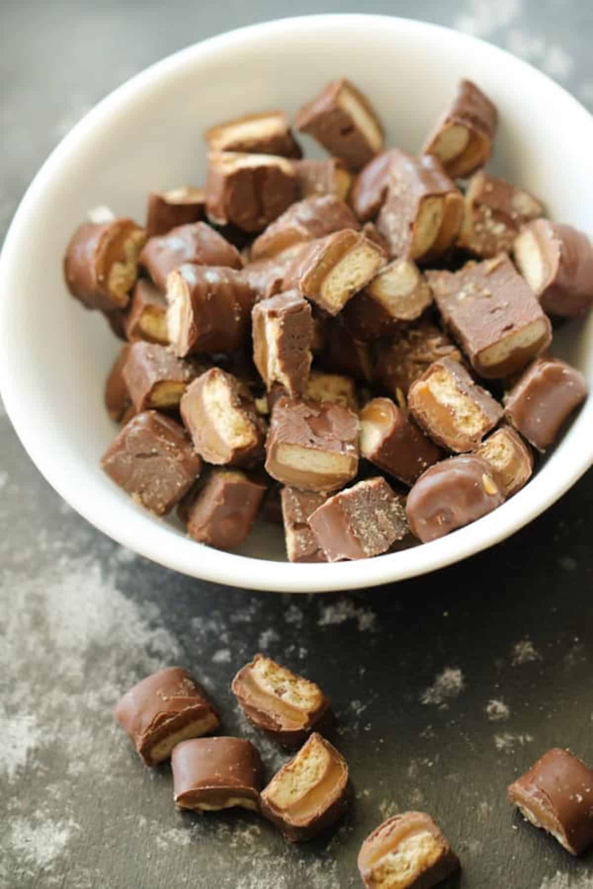A bowl with chopped up twix miniature candy bard. Some pieces laying on the counter outside of the bowl.