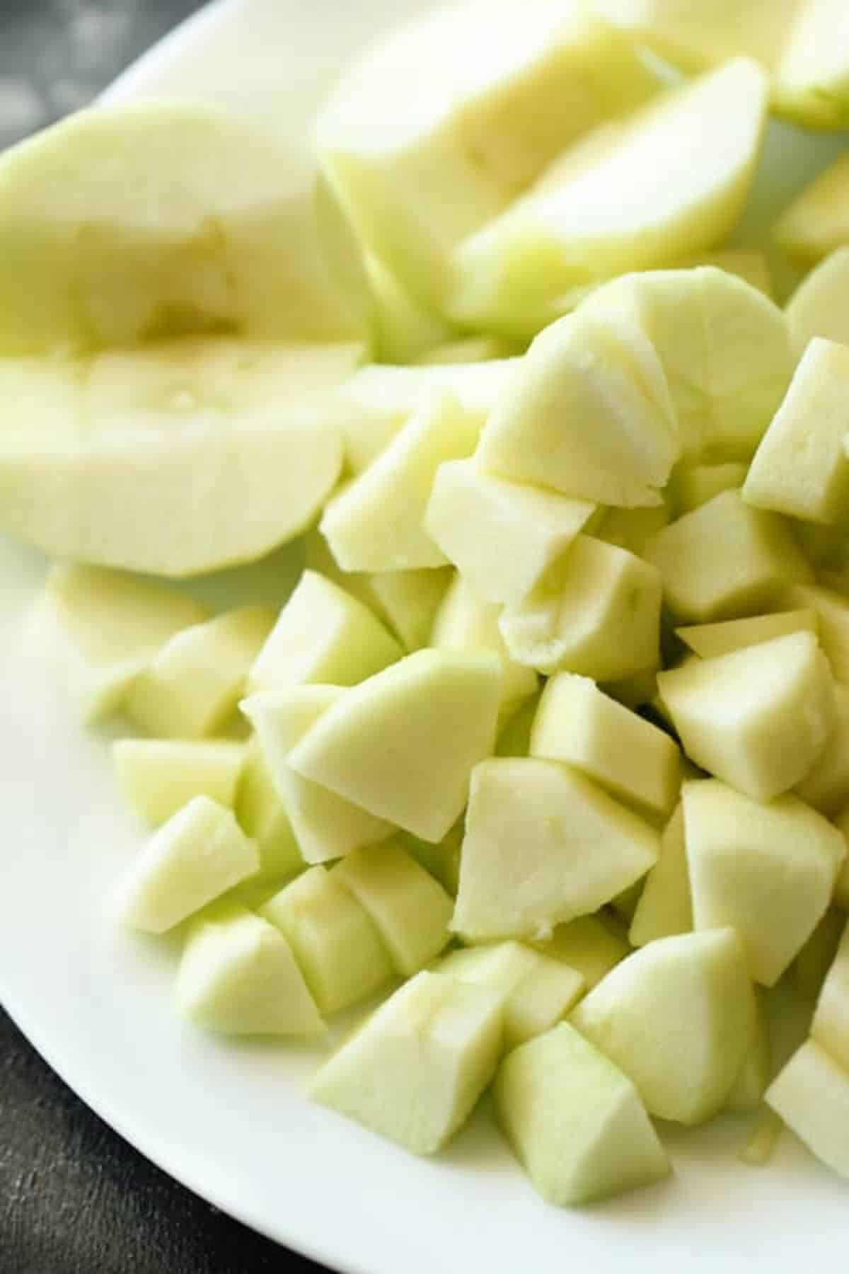 Green apples diced into cutes on a plate with some sliced apples.