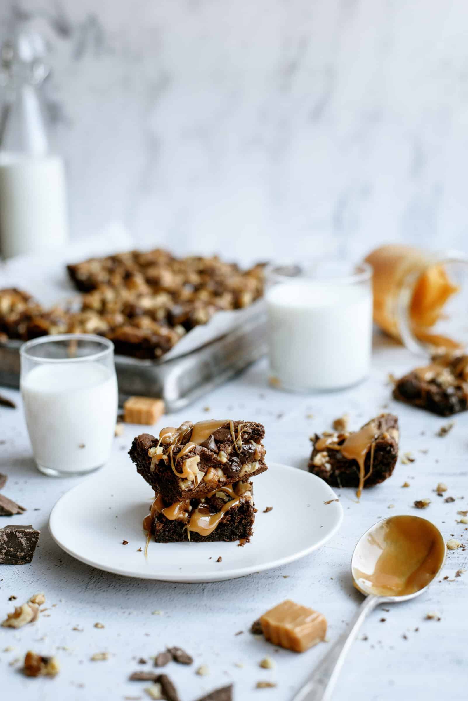 Chocolate Turtle Brownies on white dishes with glasses of milk