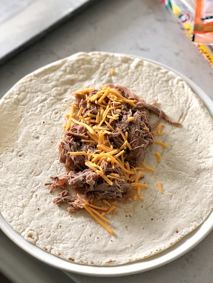 Tortilla on a plate with sweet pork filling and shredded cheese in the middle