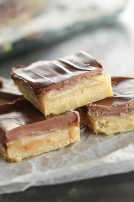 Homemade Twix Bars cut into squares and stacked on top of a serving tray.