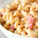 A close-up of a bowl of mac and cheese with a creamy sauce and mixed with red and green pepper pieces. The text "mexican mac 'n cheese" is in the top left corner.