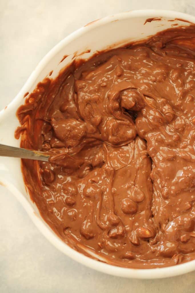 Melted chocolate, peanut butter and peanuts mixed together with a spoon in a mixing bowl.