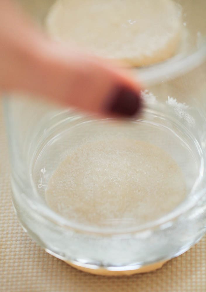 Cookie dough ball being gently flattened with a glass.