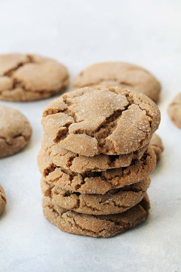 A stack of cracked, round cookies arranged on a white surface with other cookies scattered around.