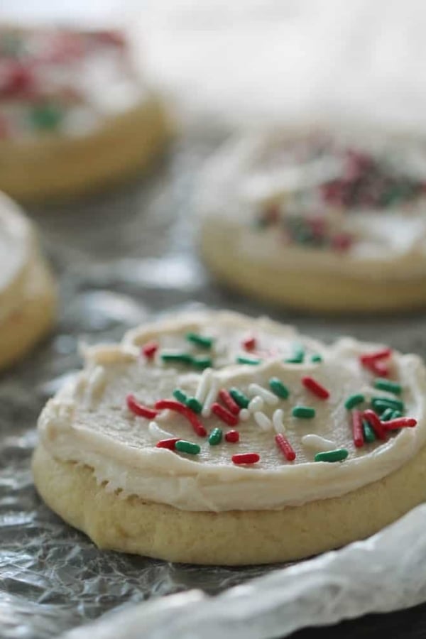 Sugar cookies with white frosting and red, green, and white sprinkles on a textured surface.