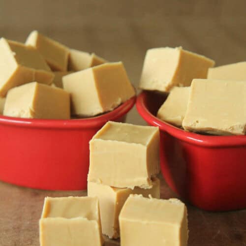 Two red bowls filled with multiple cubes of yellow fudge on a wooden surface.